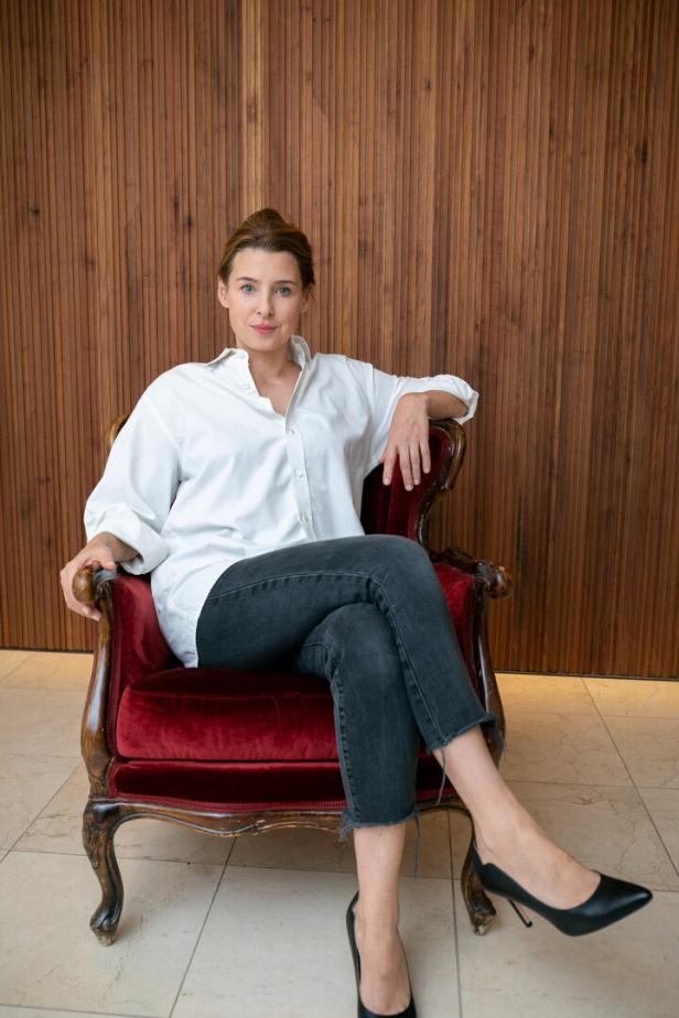 Eine Frau in Jeans und weißem Hemd sitzt in einem roten Sessel.