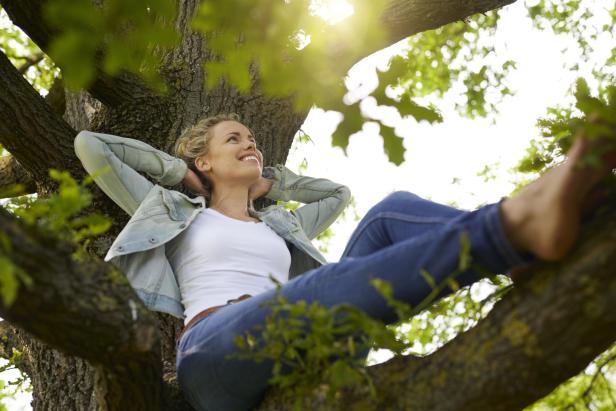 Eine blonde Frau sitzt in einem Baum und hat die Arme hinter ihrem Kopf verschränkt.