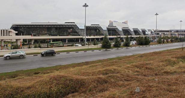 Das Flughafengebäude von Sotschi mit zwei Autos auf der Straße davor.