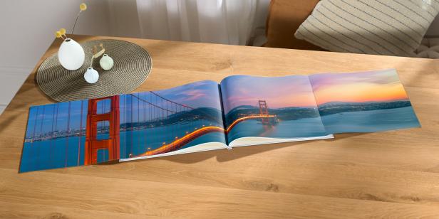 Ein ausgeklapptes Fotobuch mit einer doppelt so breiten Seite, auf der sich die Golden Gate Bridge im Sonnenuntergang befindet.