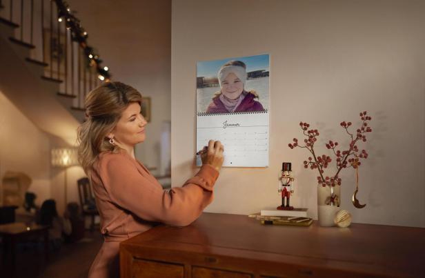 Eine Frau steht vor einem Fotokalender. Dahinter ist Weihnachtsbeleuchtung.