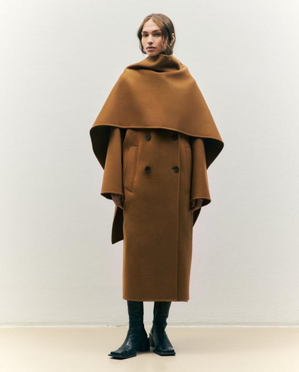 Eine Frau trägt einen langen, braunen Mantel mit einem übergroßen Kragen und schwarze Stiefel.