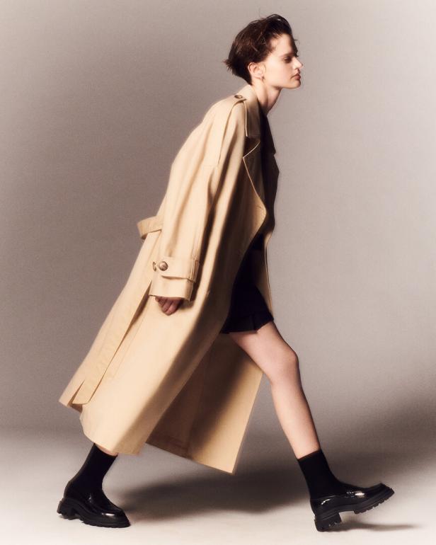 Eine Frau geht in einem beigen Trenchcoat und schwarzen Schuhen von Hogan.