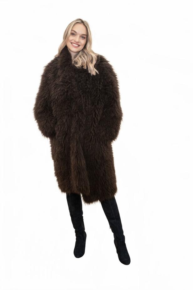 Eine blonde Frau trägt einen langen, braunen Fellmantel und schwarze Stiefel.