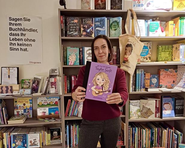Eine Frau steht in einem Buchladen und hält eine Biografie über Taylor Swift in der Hand.