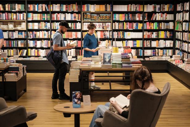 In einer Buchhandlung stöbern Kunden zwischen den vollen Bücherregalen.
