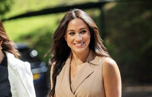 Meghan Markle lächelt in einem beigefarbenen Kleid.