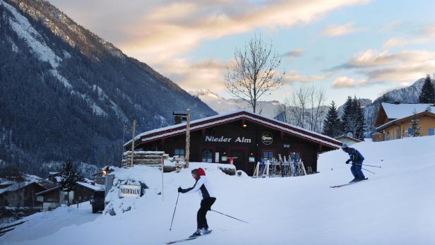 Skifahrer vor der „Nieder Alm“ Hütte in einer verschneiten Winterlandschaft.