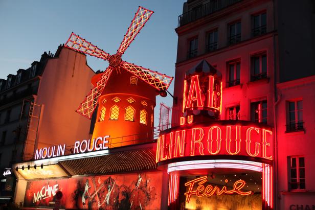 Das Moulin Rouge in Paris mit seiner ikonischen roten Windmühle, beleuchtet in der Abenddämmerung.