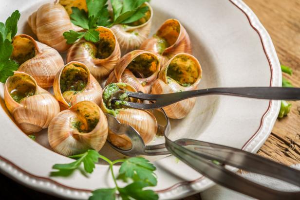 Eine Portion Schnecken mit Kräuterbutter wird mit einer Zange serviert.