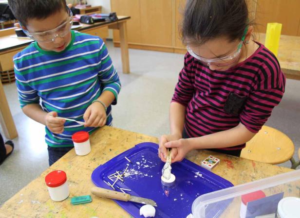 Zwei Kinder mit Schutzbrillen basteln an einem Tisch mit Werkzeugen und Materialien.