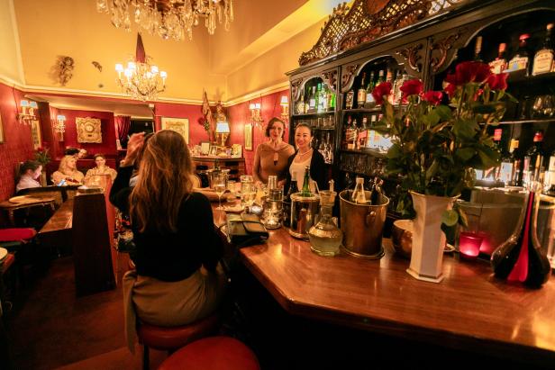 In einer Bar stehen zwei Barkeeper hinter der Theke, während Gäste an Tischen sitzen.