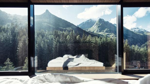 Blick aus einem Fenster auf eine Berglandschaft mit einem Bett im Vordergrund.