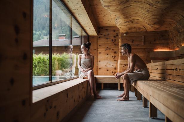 Ein Mann und eine Frau sitzen in Handtücher gehüllt in einer Sauna.