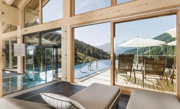 Blick aus dem Innenbereich eines Spas auf einen Außenpool mit Bergblick.