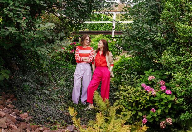 Zwei Frauen stehen in einem üppigen Garten und schauen sich an.