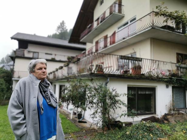 Eine ältere Frau steht vor einem mehrstöckigen Haus mit Balkonen.