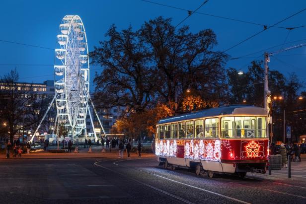 Ein weihnachtlich geschmückte Straßenbahn fährt vor einem beleuchteten Riesenrad.
