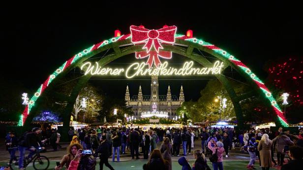 Der Wiener Christkindlmarkt mit dem Rathaus im Hintergrund ist hell erleuchtet.
