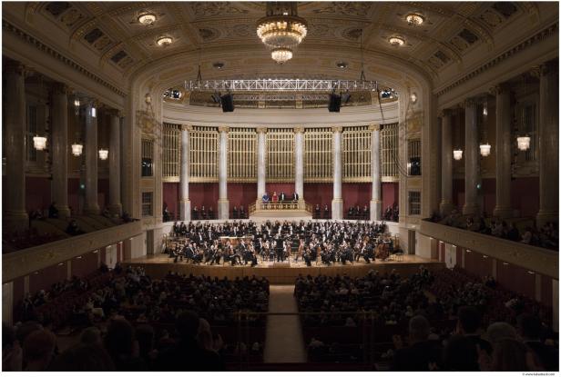 Ein pompöser Saal mit Publikum. Auf der Bühne befindet sich ein Orchester.