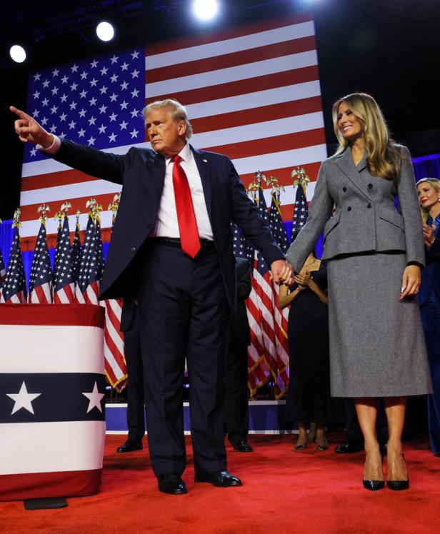 Donald Trump und Melania Trump stehen vor amerikanischen Flaggen.