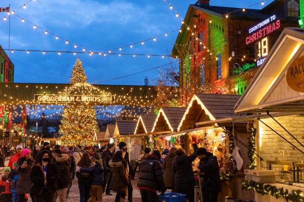 Ein Weihnachtsmarkt mit Menschen, Buden und einem großen Weihnachtsbaum unter Lichterketten.