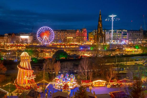 Der Weihnachtsmarkt in Edinburgh mit Riesenrad und anderen Fahrgeschäften bei Nacht.