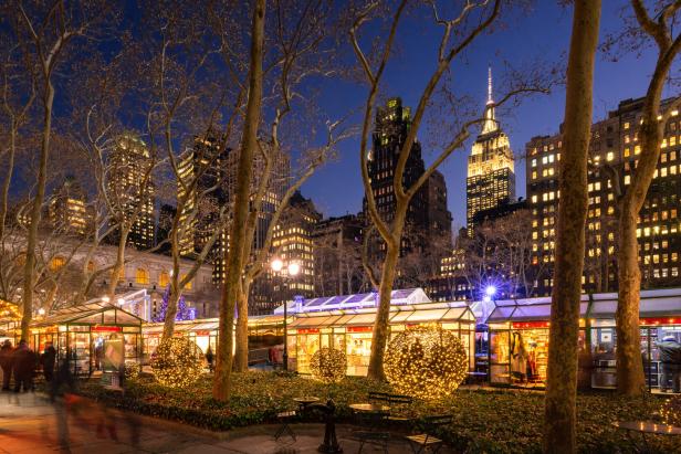 Der Weihnachtsmarkt im Bryant Park in New York City bei Nacht mit dem Empire State Building im Hintergrund.