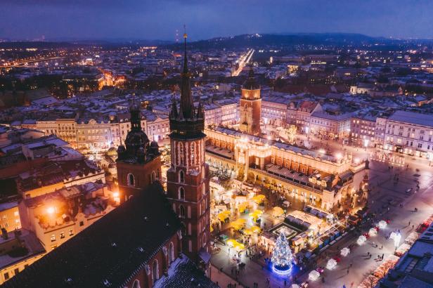 Ein nächtlicher Blick auf den verschneiten Marktplatz von Krakau mit Weihnachtsbaum und beleuchteten Ständen.