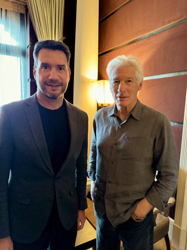 Richard Gere posiert mit einem Mann in einem grauen Sakko.