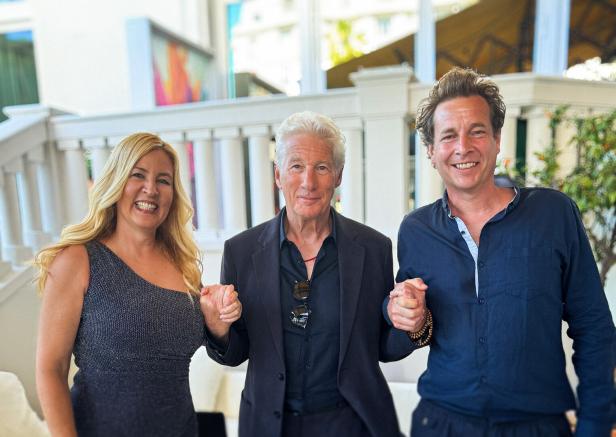 Richard Gere posiert mit zwei weiteren Personen, die Hände haltend, für ein Foto.