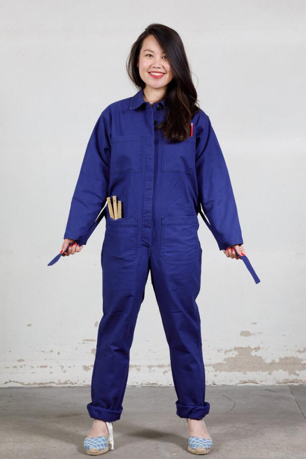 Eine Frau in einem blauen Vétra-Arbeitsanzug steht vor einer Wand.