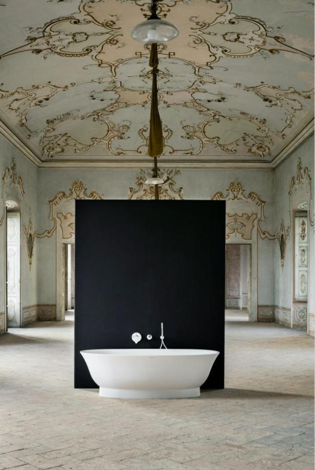 Eine freistehende Badewanne vor einer schwarzen Wand in einem verzierten Raum.