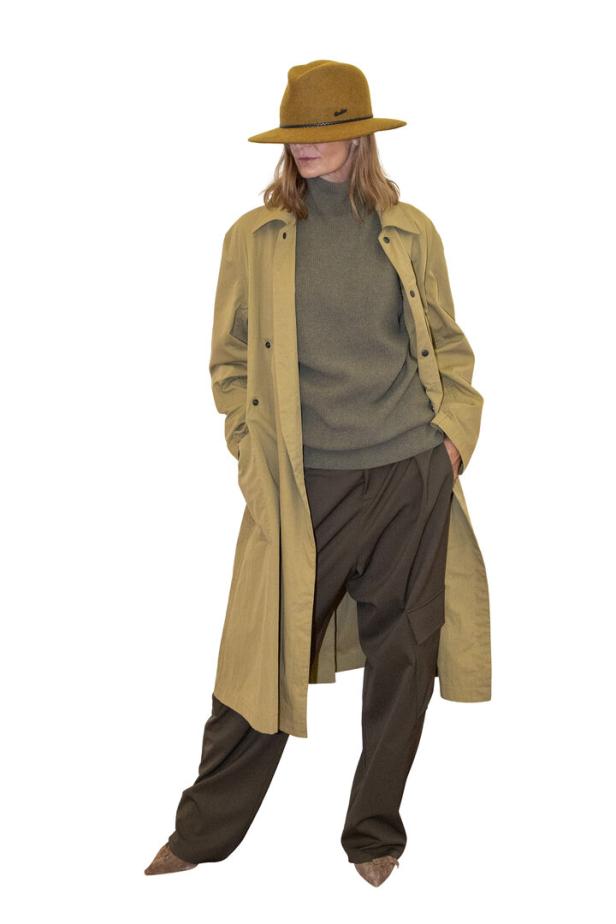 Eine Frau mit Hut, Trenchcoat, Rollkragenpullover und weiter Hose posiert.
