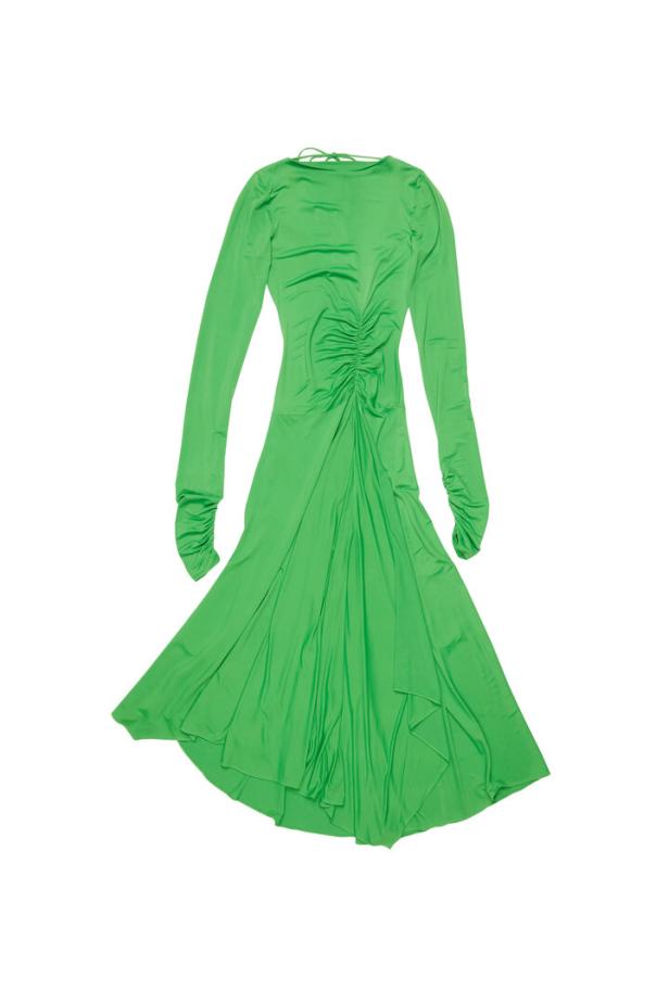 Ein grünes, langärmeliges Kleid mit Raffungen im Rockteil liegt auf einem weißen Hintergrund.