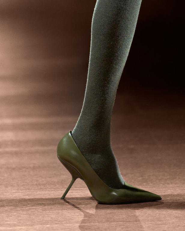 Ein Bein mit Strumpf und ein grüner High Heel mit einem dünnen Absatz.