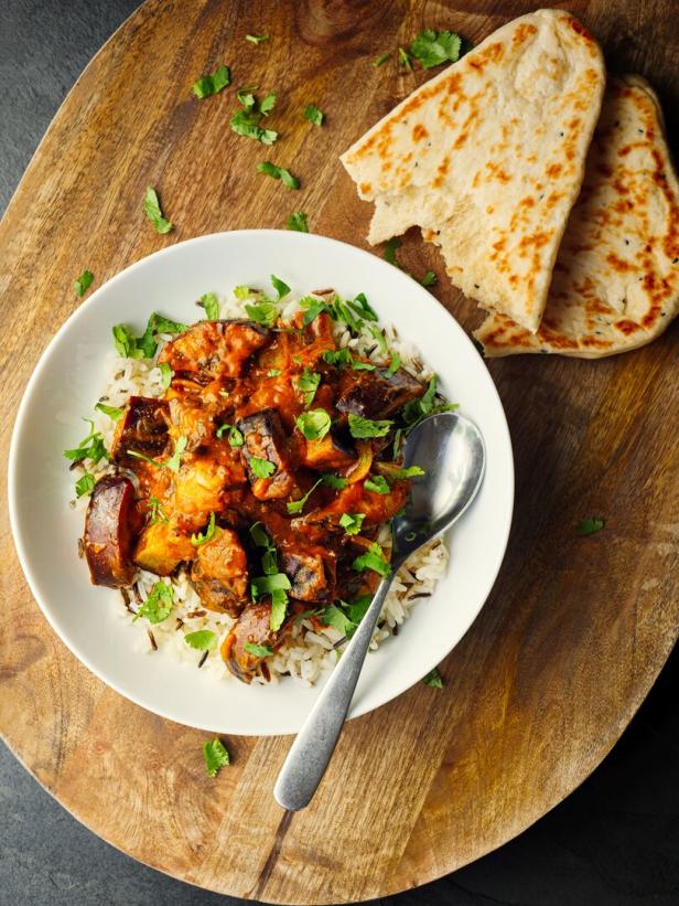 Ein Teller mit Auberginen-Curry auf Reis, garniert mit Koriander, zusammen mit Naan-Brot.