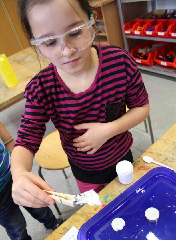 Ein Mädchen mit Schutzbrille experimentiert mit einer Wäscheklammer und Kerzen.