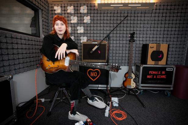 Mira Lu Kovacs sitzt mit einer Gitarre in einem Aufnahmestudio.