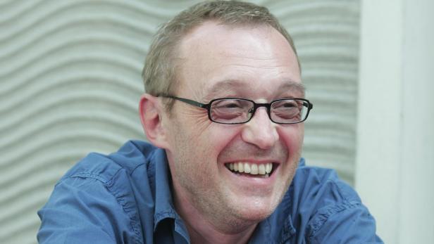 Ein lachender Mann mit Brille und blauem Hemd.