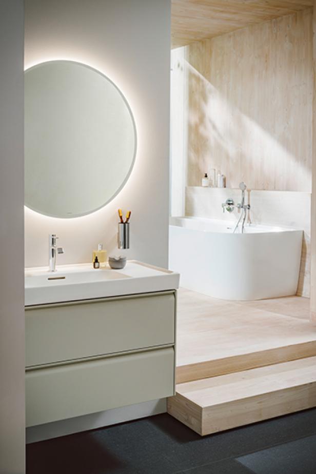 Ein modernes Badezimmer mit einem runden Spiegel, einem Waschtisch und einer Badewanne.