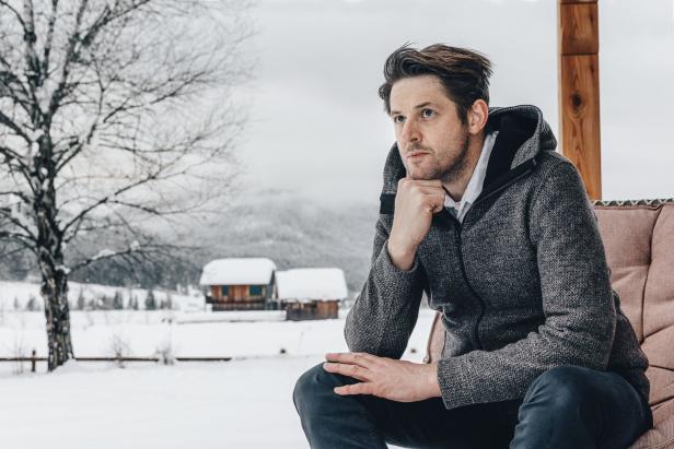 Ein Mann sitzt im Winter vor einer Hütte und denkt nach.
