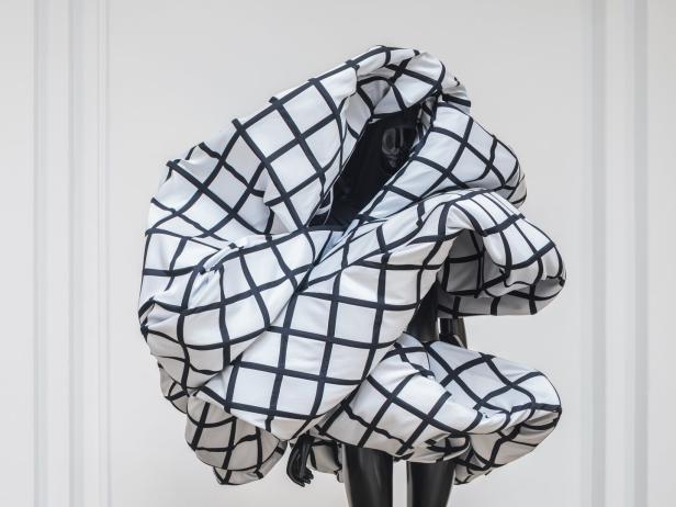 Ein weißes, voluminöses Kleid mit schwarzem Karomuster auf einer Schaufensterpuppe.