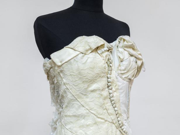 Ein weißes Spitzenkleid mit Knöpfen auf einer schwarzen Schneiderpuppe.