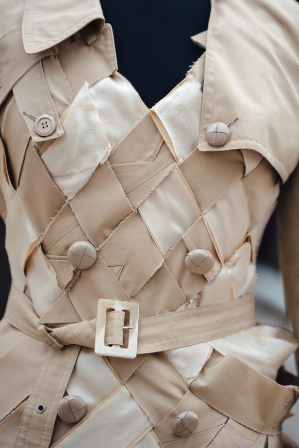 Ein beigefarbener Trenchcoat mit einem gewebten Design und einem Gürtel mit Schnalle.