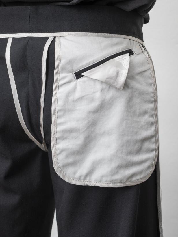 Detailaufnahme einer schwarzen Hose mit einer hellgrauen, aufgesetzten Tasche.