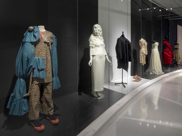 Eine Ausstellung mit verschiedenen Kleidungsstücken, darunter ein Leopardenmuster-Anzug und ein weißes, hochgeschlossenes Kleid.
