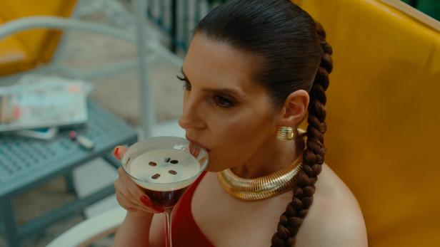 Eine Frau mit Zopf trinkt einen Espresso Martini mit Kaffeebohnen.