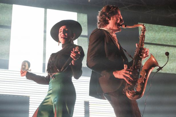 Eine Sängerin mit Hut und ein Saxophonist treten auf einer Bühne auf.