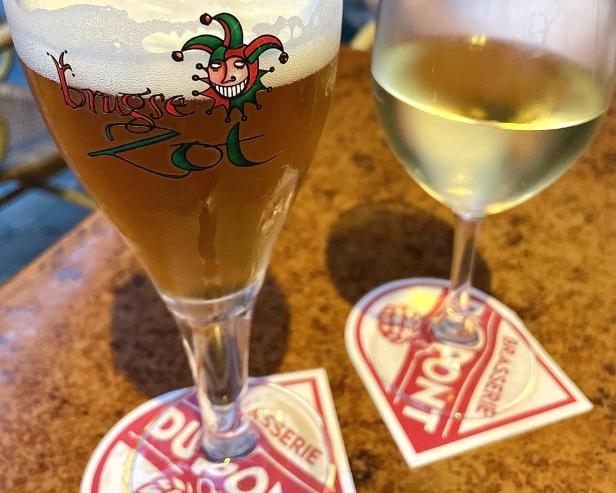 Ein Glas belgisches Bier der Marke „Brugse Zot“ und ein Glas Weißwein stehen auf dem Tisch.